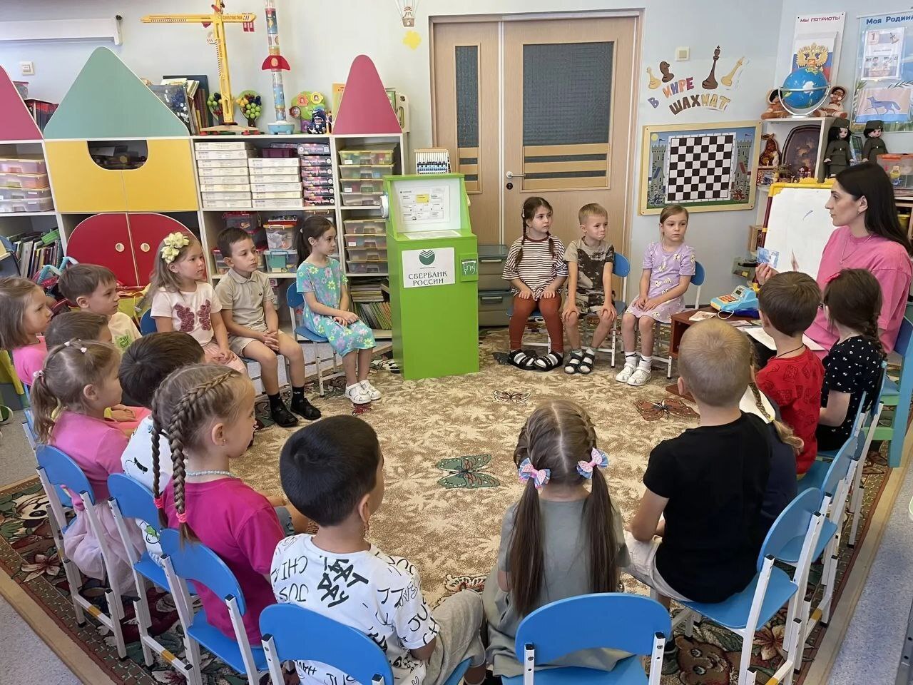 На фото дети сидят в кругу, воспитатель проводит тематическое занятие на тему Что такое деньги?