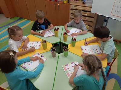 На фото дети выполняют за столом  задания в рабочих тетрадях по дополнительной программе На пороге школы