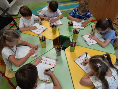 На фото дети выполняют за столом  задания в рабочих тетрадях по дополнительной программе На пороге школы